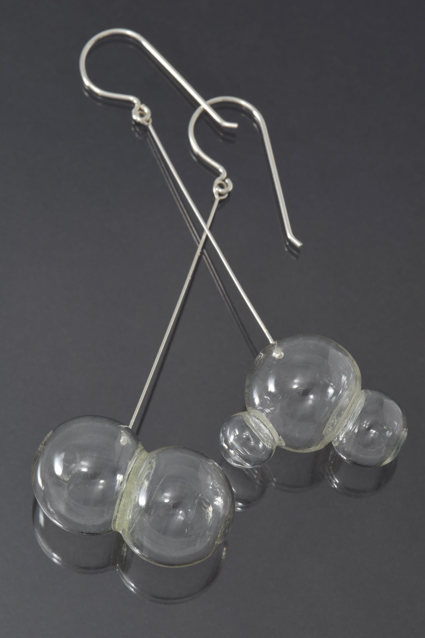 One pair and one triplet of glass bubbles hang at the end of a long, straight piece of silver on a fishhook style earwire.