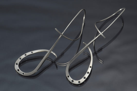 Sterling silver earrings made of wire that loops around and down.  Circles, slightly graduated in size are cut out along the bottom section of the earring, each with shiny beveled edges.