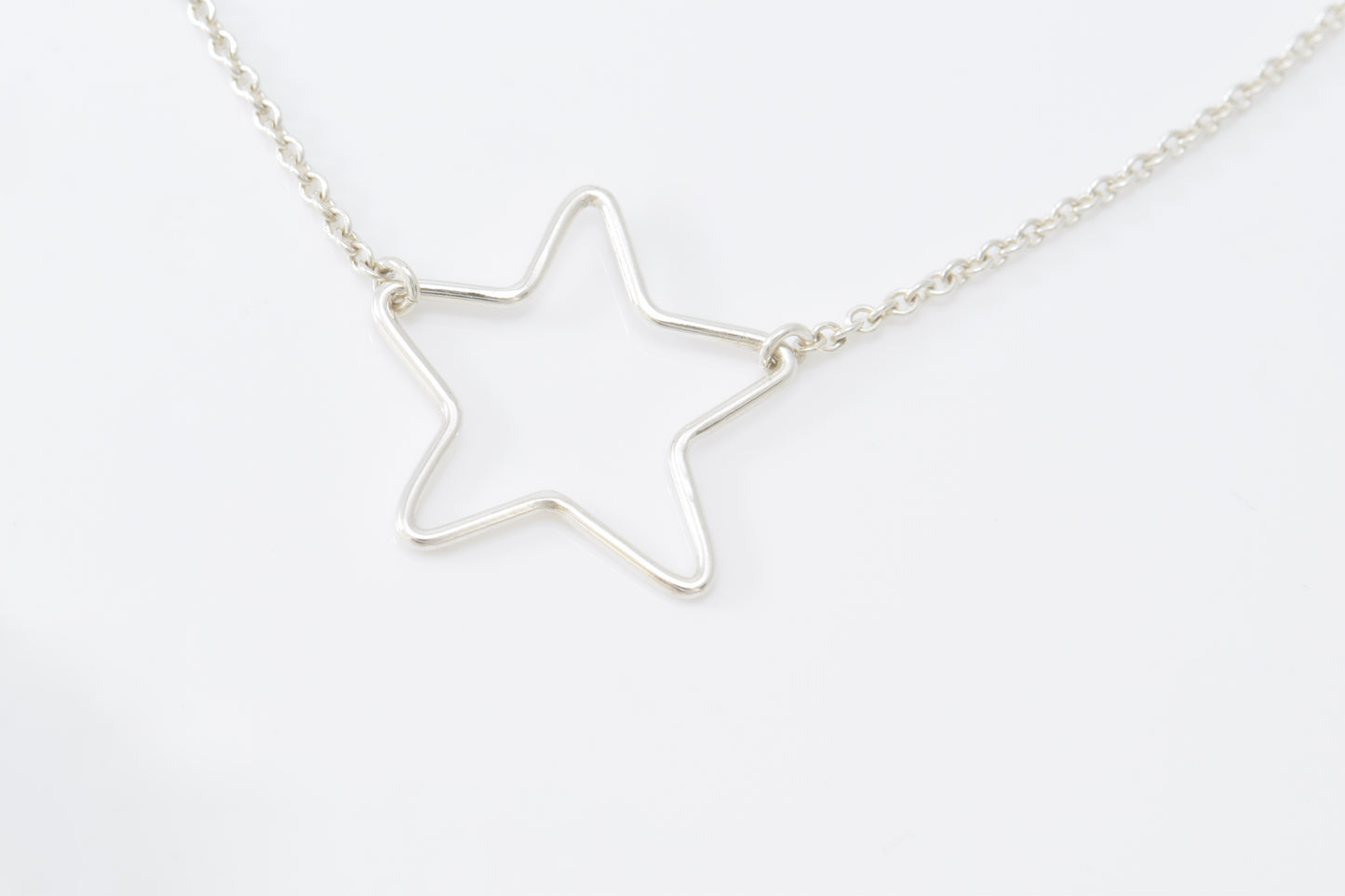 Silver star-shaped pendant inline on a chain against a white background