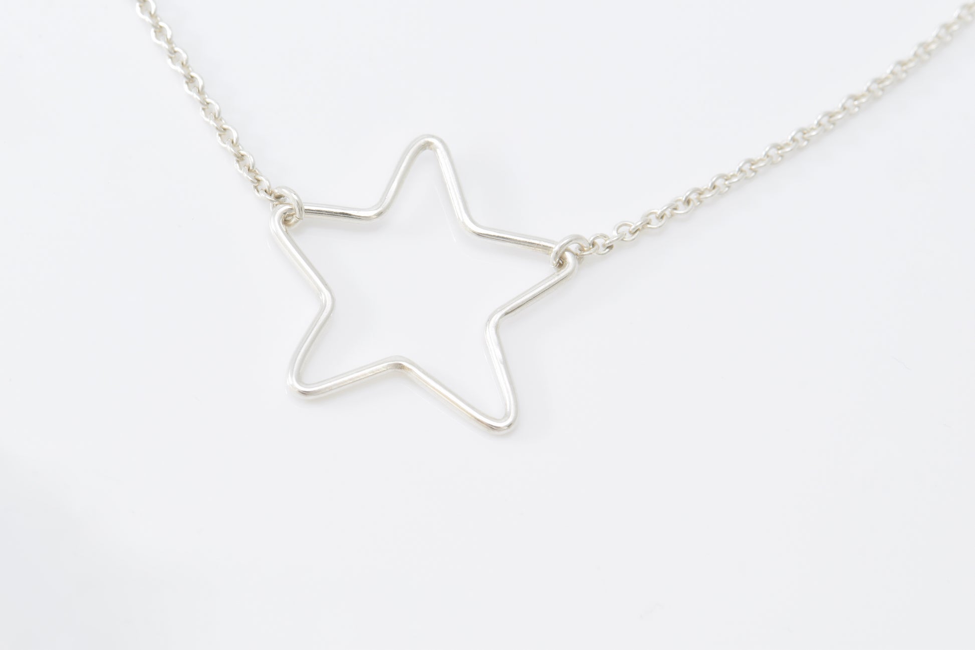 Silver star-shaped pendant inline on a chain against a white background