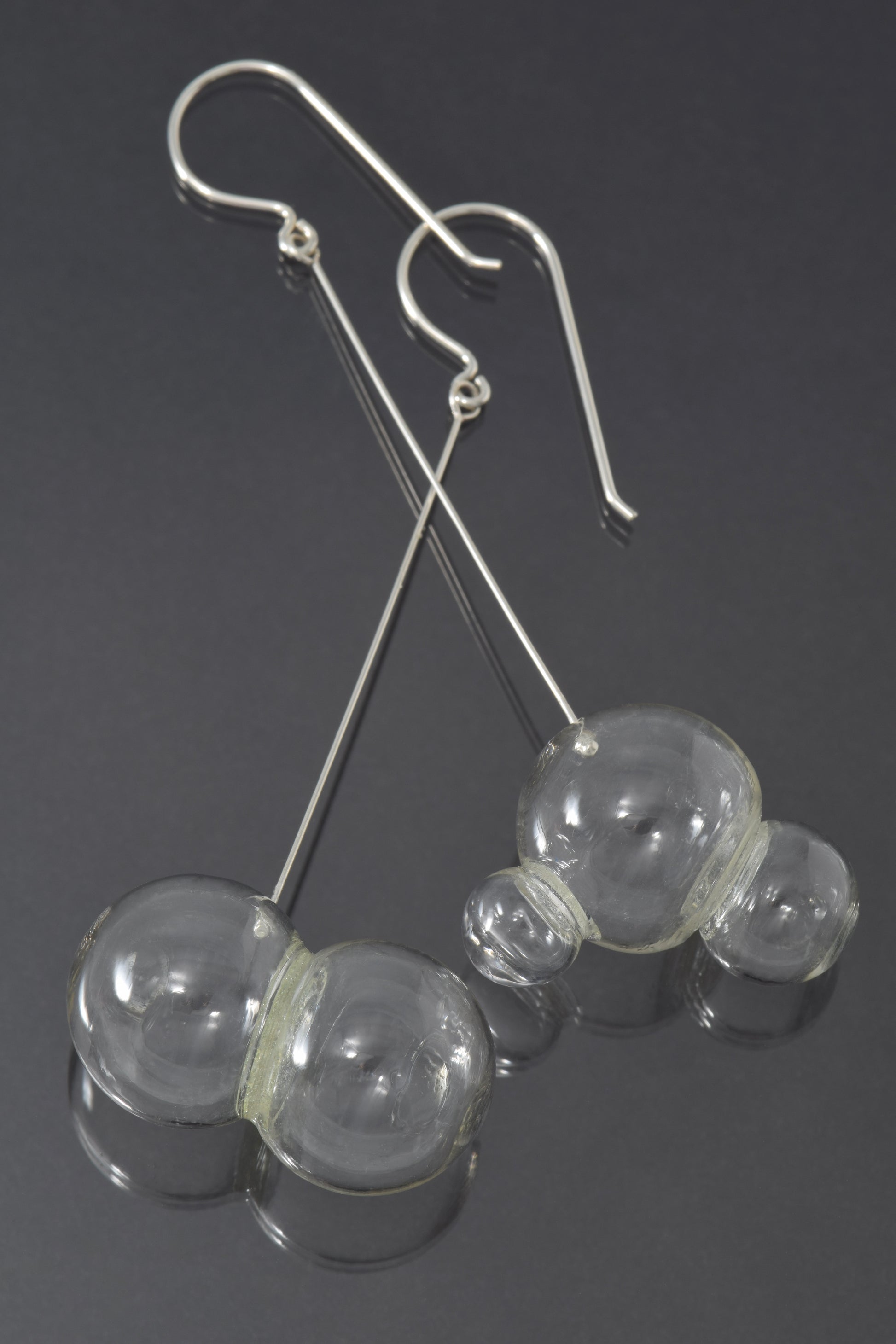 One pair and one triplet of glass bubbles hang at the end of a long, straight piece of silver on a fishhook style earwire.