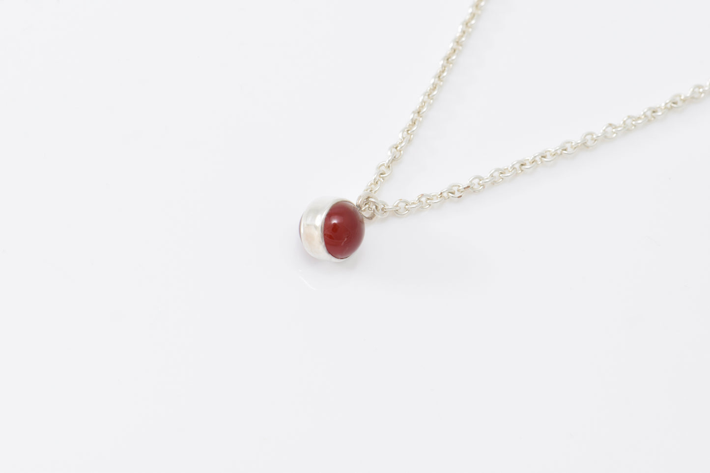 Lightweight cable chain with red carnelain spherical pendant on white background.