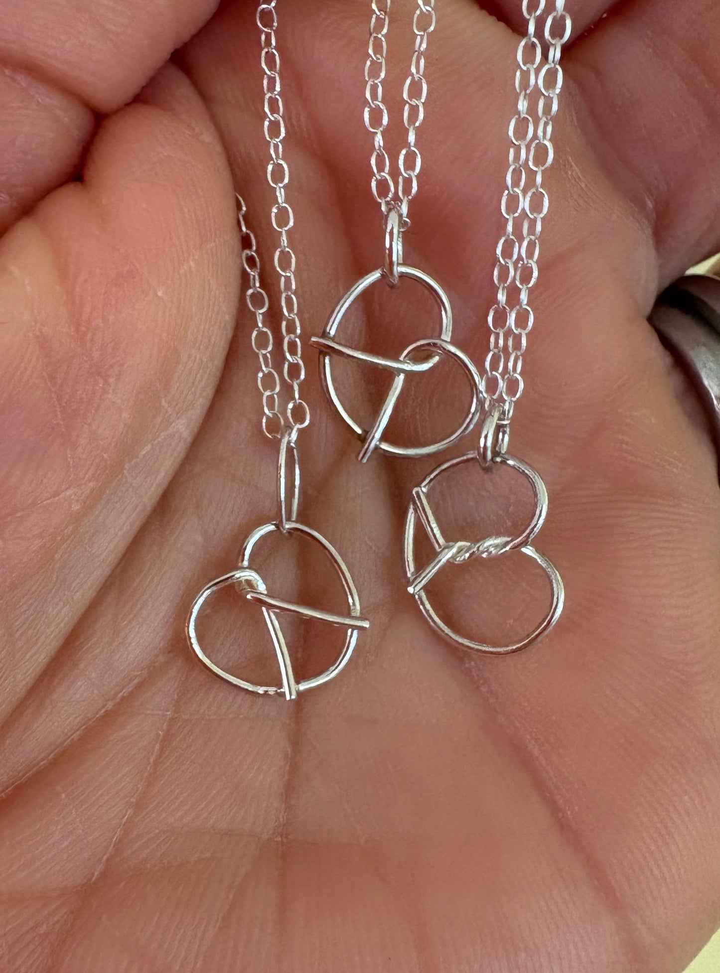 Silver pretzel-shaped necklace and chain held in a hand against a neutral background