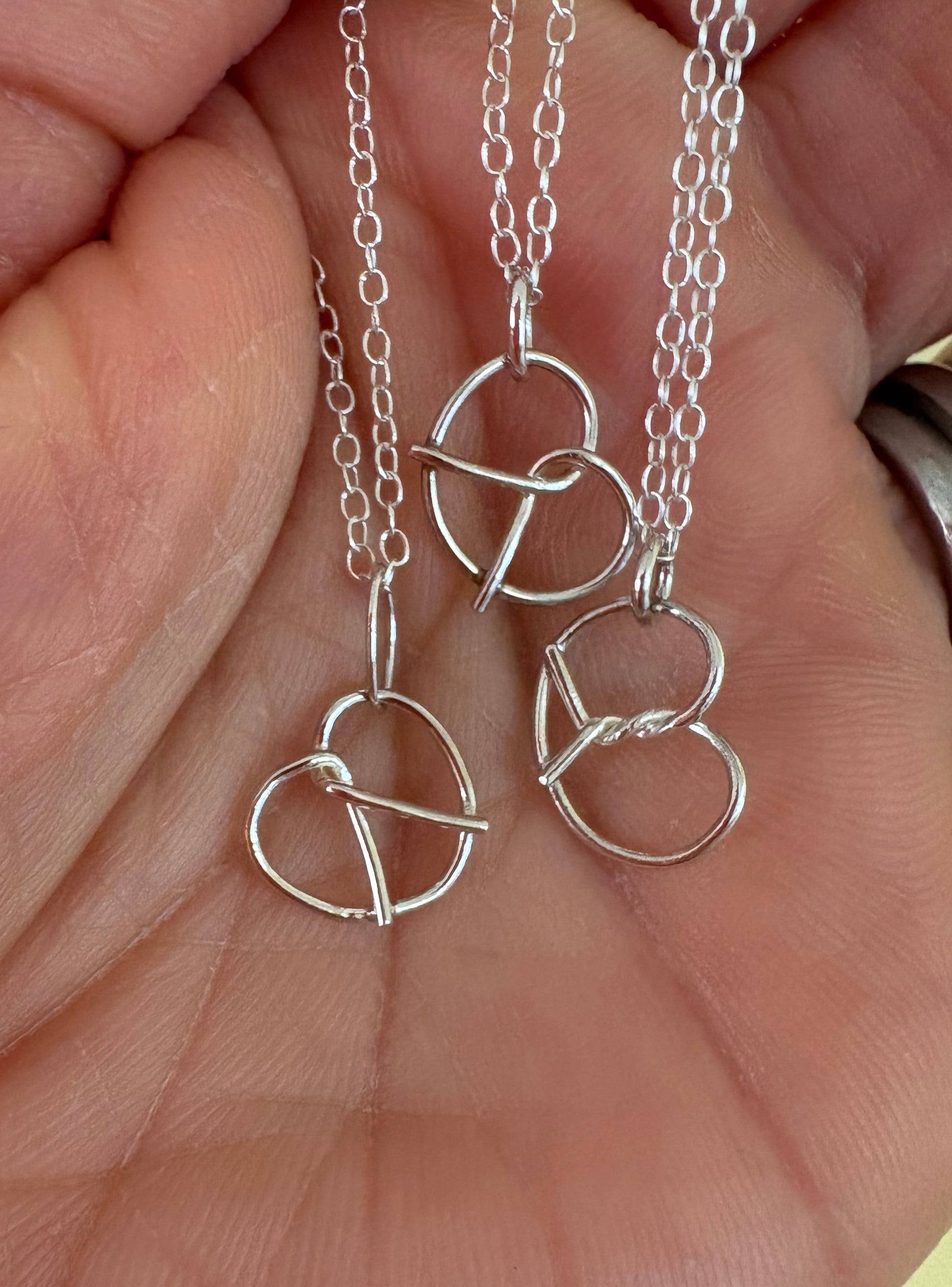 Silver pretzel-shaped necklace and chain held in a hand against a neutral background