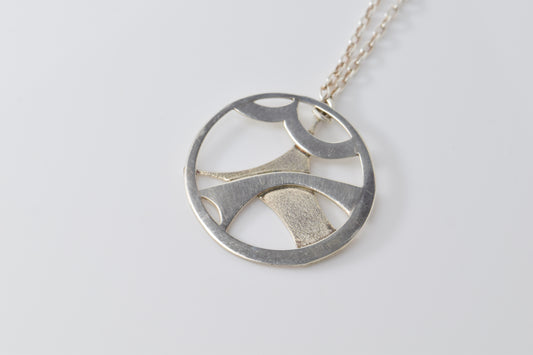 Silver necklace with a circular pendant on a white
 background