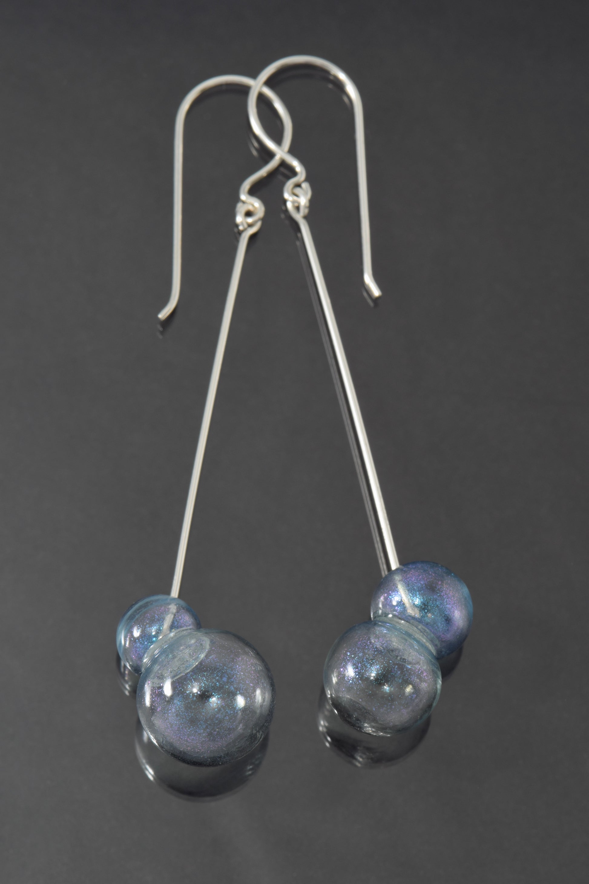 Lightly blue iridescent pairs of glass bubbles dangle at the ends of long, straight silver earrings.