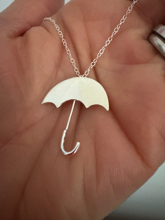 Sterling silver umbrella pendant on lightweight silver chain, held in a hand