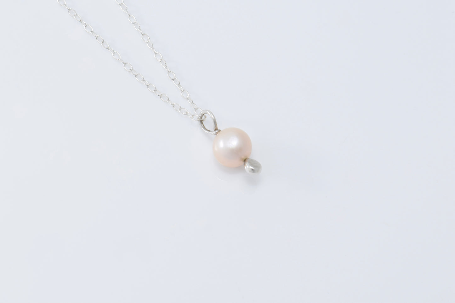A single pearl pendant with a silver drop below it on a lightweight silver chain with a white background
