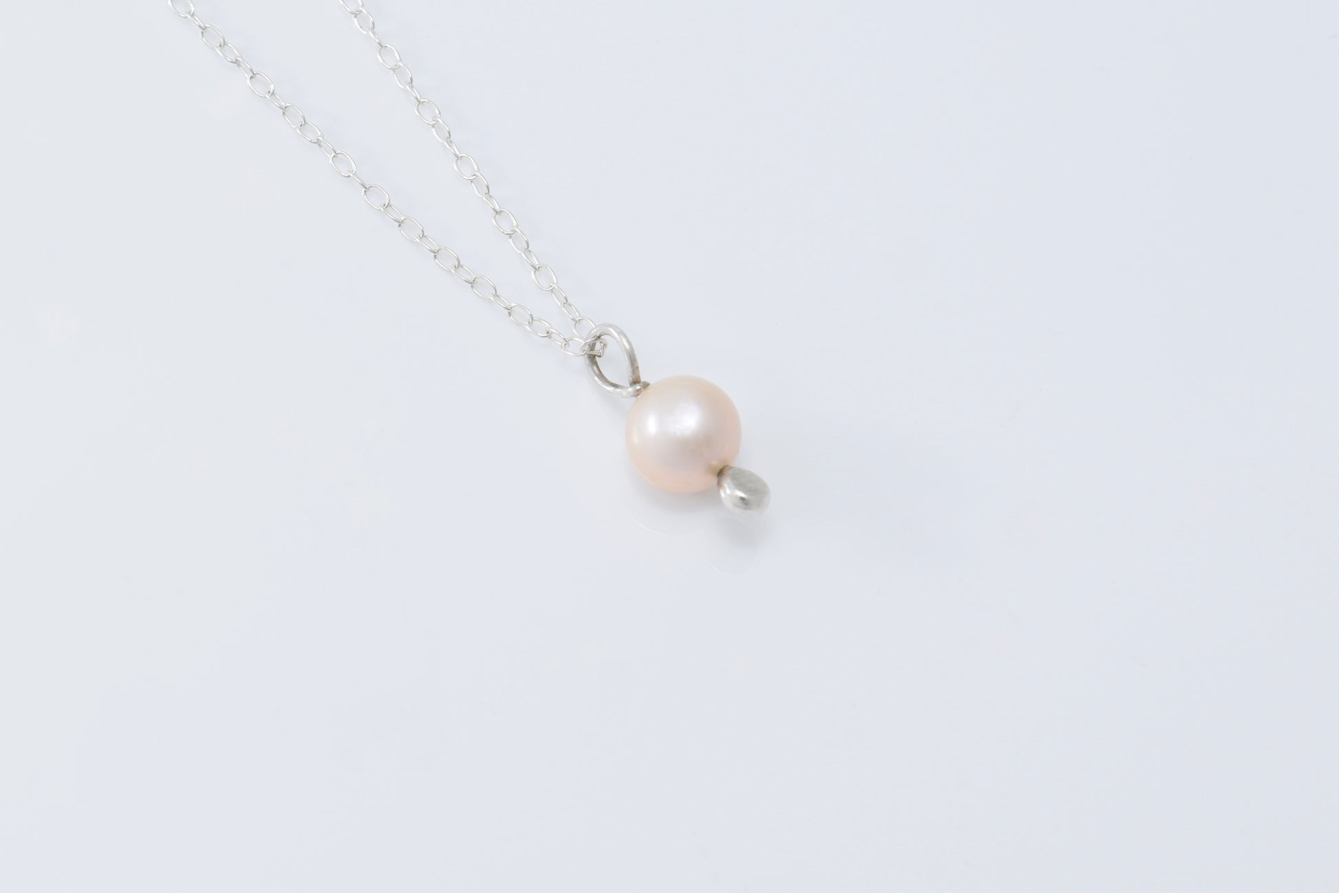A single pearl pendant with a silver drop below it on a lightweight silver chain with a white background