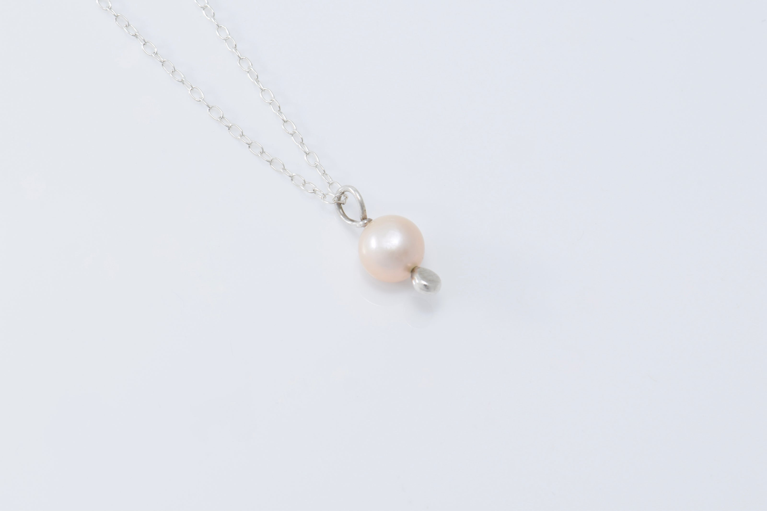 A single pearl pendant with a silver drop below it on a lightweight silver chain with a white background
