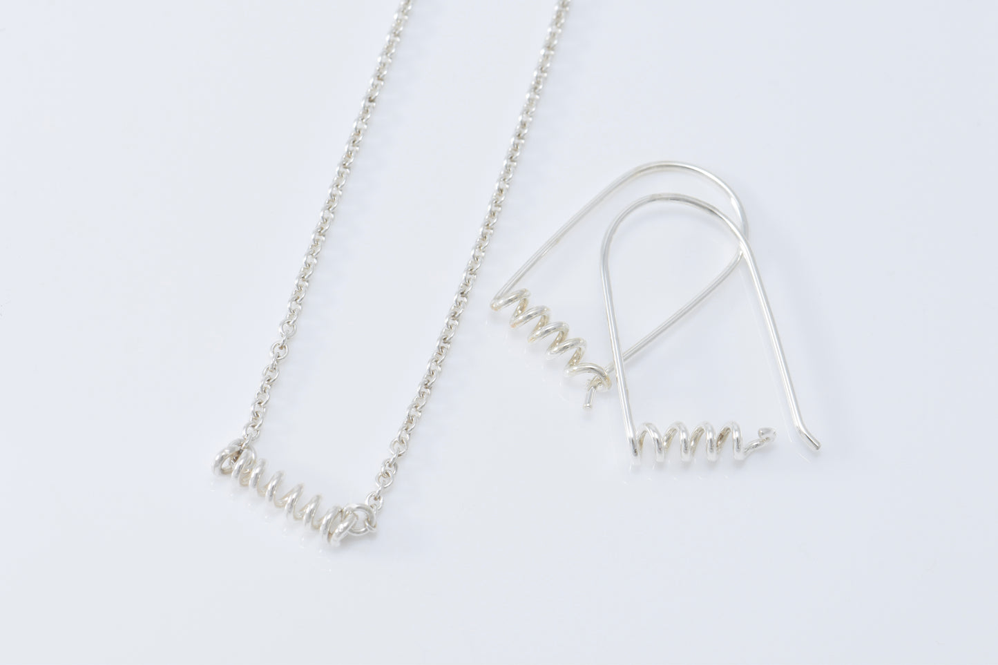 Necklace and earrings each with skinny spirals on white background