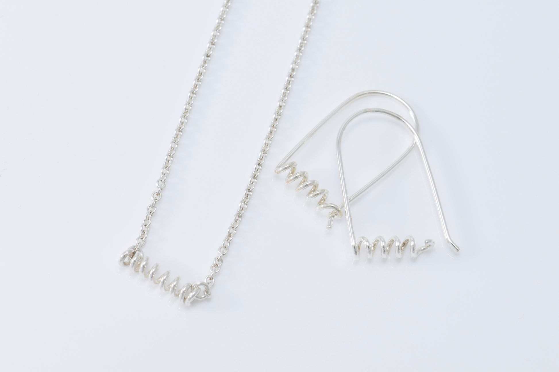 Necklace and earrings each with skinny spirals on white background