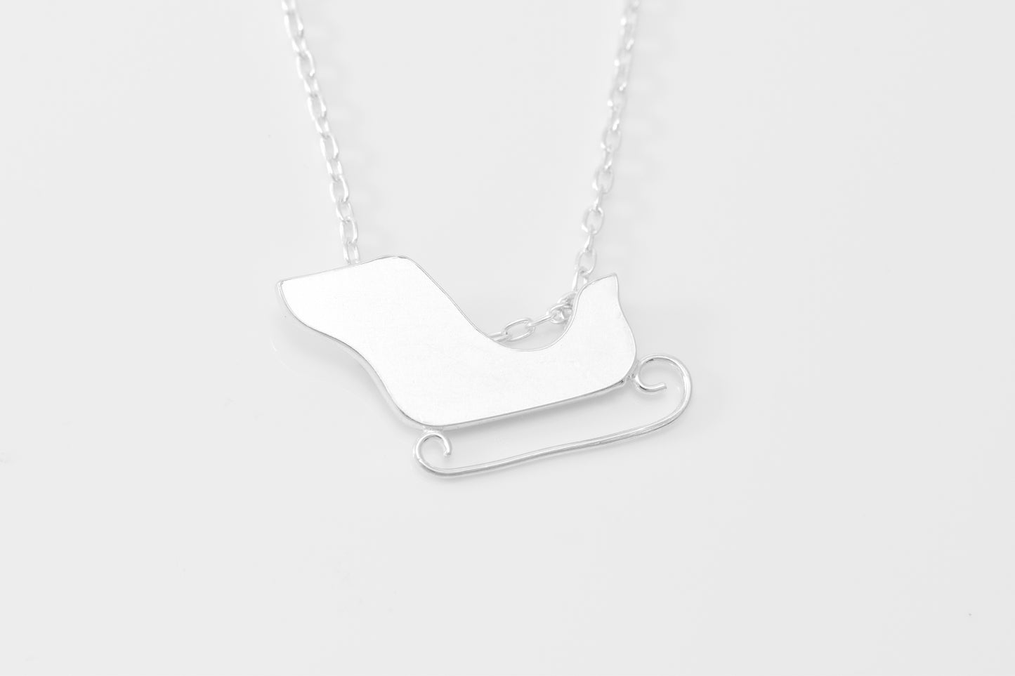 Silver sleigh pendant on a chain against a white background