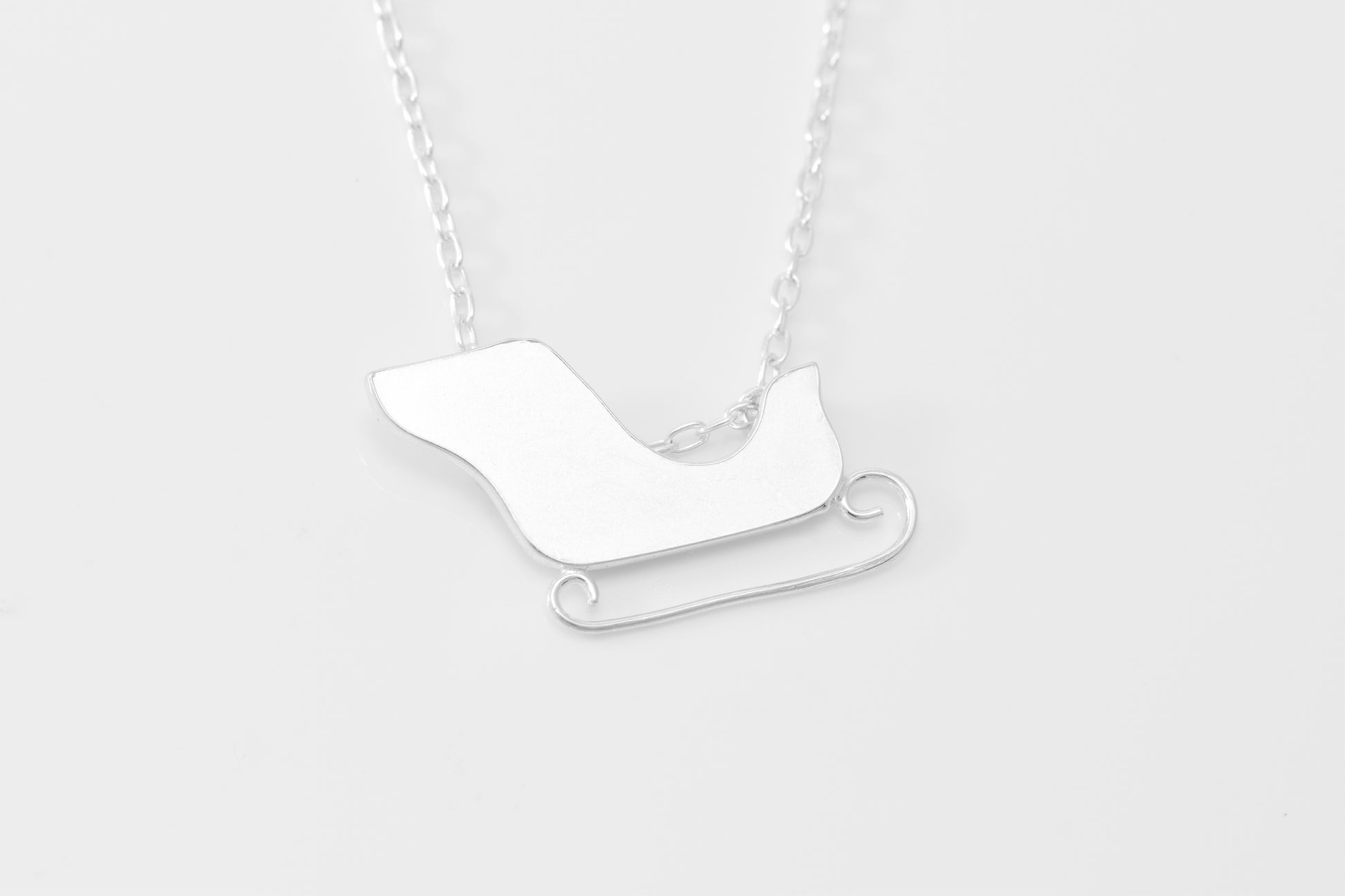 Silver sleigh pendant on a chain against a white background