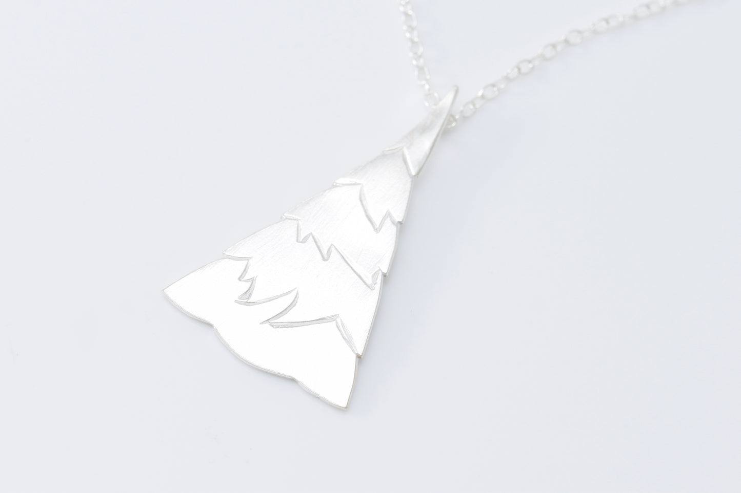 Silver evergreen tree pendant with jagged tiers on cable chain with white background