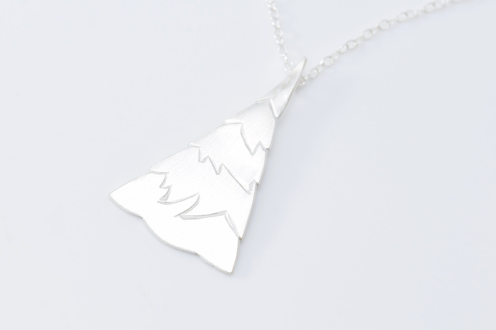 Silver evergreen tree pendant with jagged tiers on cable chain with white background
