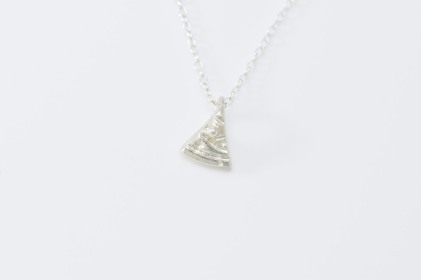 Tiny silver triangle Christmas tree with carved garland and ball ornaments on able chain.